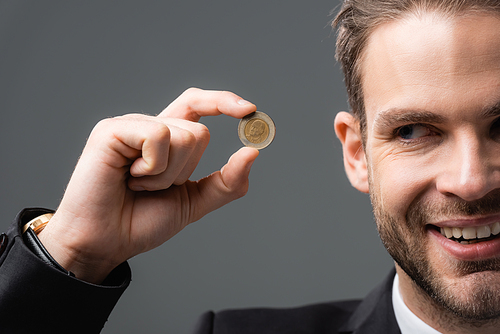 cropped view of joyful businessman showing coin isolated on grey