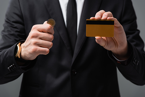 partial view of businessman showing credit card and coin on blurred background isolated on grey