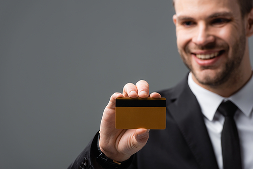 happy businessman showing credit card on blurred background isolated on grey