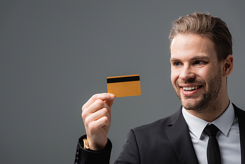 smiling businessman holding credit card isolated on grey