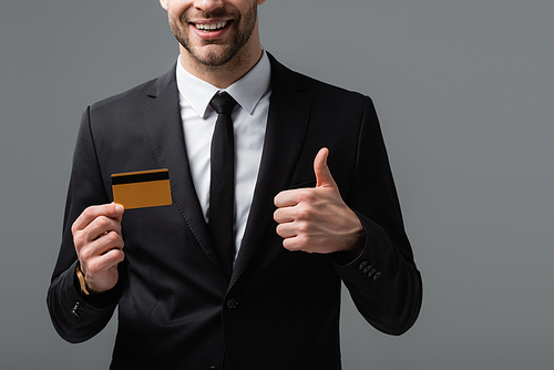 partial view of joyful manager showing thumb up and credit card isolated on grey