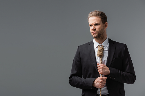 tense businessman with rope around neck looking away isolated on grey