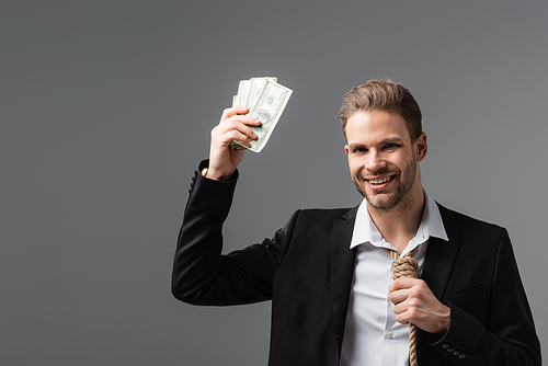 cheerful businessman with rope instead of tie holding dollars isolated on grey