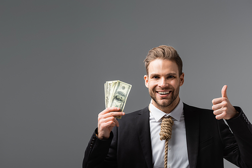 cheerful businessman with tie made of rope holding dollars and showing like isolated on grey