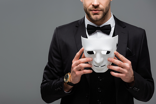 cropped view of businessman in black suit holding face mask isolated on grey