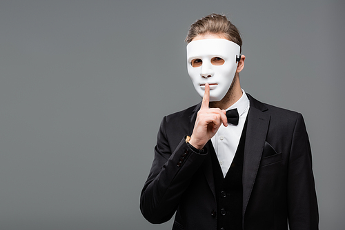 young businessman in face mask showing secret gesture isolated on grey