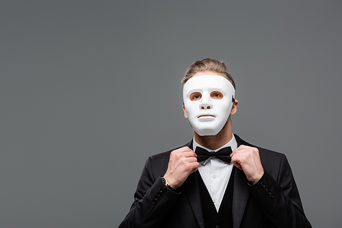 elegant businessman in face mask adjusting bow tie isolated on grey