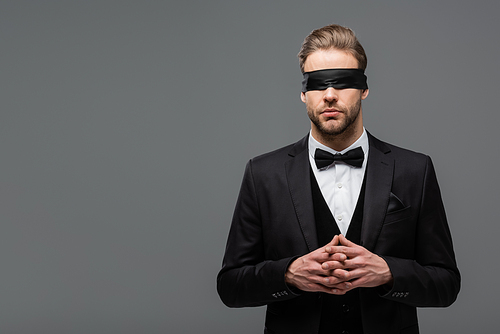 young businessman in blindfold standing with joined fingers isolated on grey