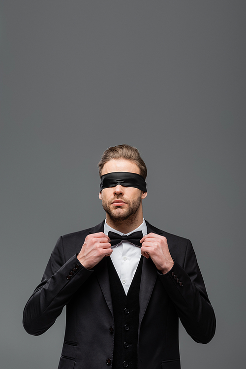 blindfolded businessman adjusting bow tie isolated on grey