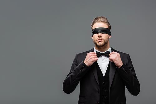 elegant, blindfolded businessman adjusting bow tie isolated on grey