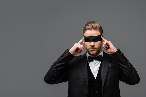 elegant businessman adjusting blindfold isolated on grey