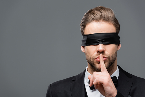 businessman in blindfold showing hush sign isolated on grey