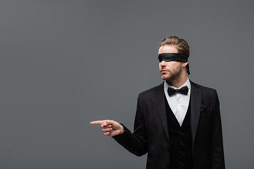 blindfolded businessman in black suit pointing away with finger isolated on grey