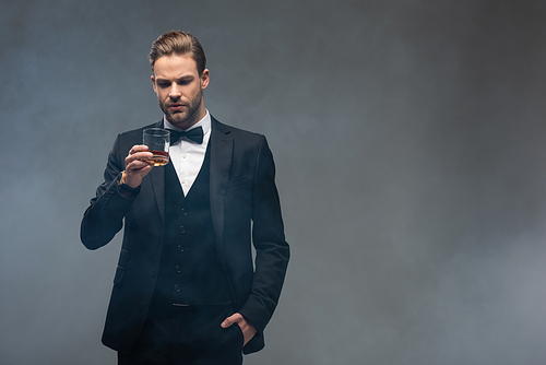 elegant businessman holding glass of whiskey on grey background with smoke