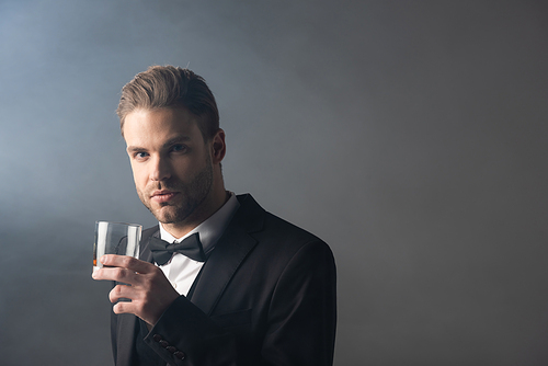 successful businessman  while holding glass of whiskey on grey background with smoke