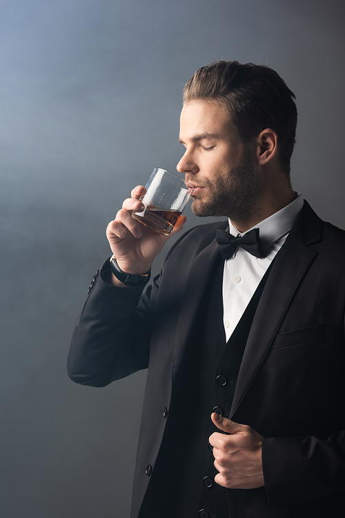 successful businessman drinking whiskey with closed eyes on grey background with smoke