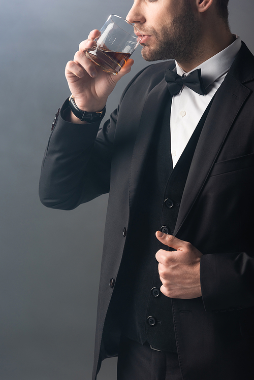 cropped view of elegant businessman drinking whiskey on grey background with smoke