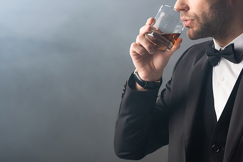 partial view of elegant businessman drinking whiskey on grey background with smoke
