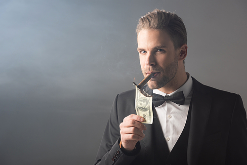 businessman lighting cigar from dollar banknote while  on grey background with smoke