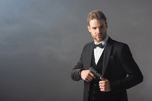 confident businessman hiding gun under blazer on grey background with smoke
