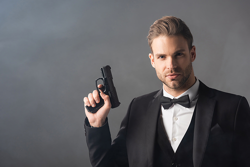elegant businessman  while holding weapon on grey background with smoke