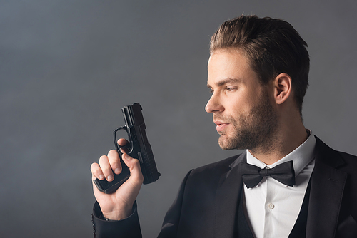young, confident businessman holding weapon on grey background with smoke