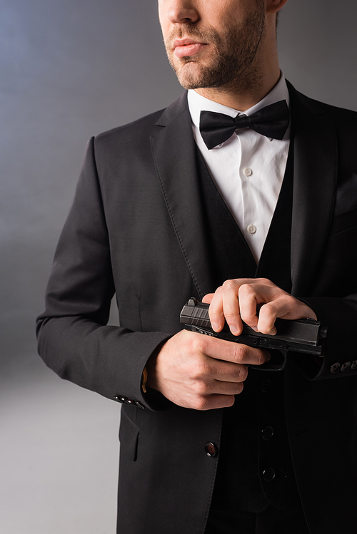 cropped view of elegant businessman holding gun on grey background with smoke