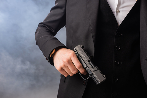 partial view of businessman with gun on grey background with smoke