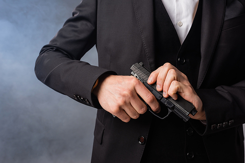 partial view of armed businessman in black suit on grey background with smoke