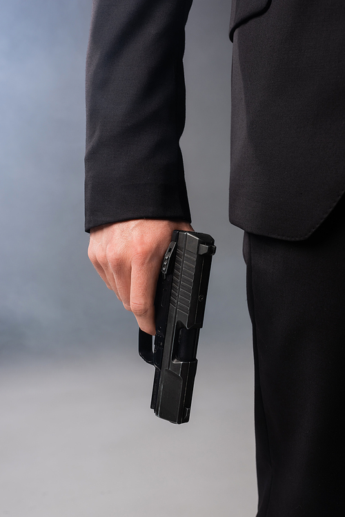 cropped view of businessman with gun on grey background with smoke