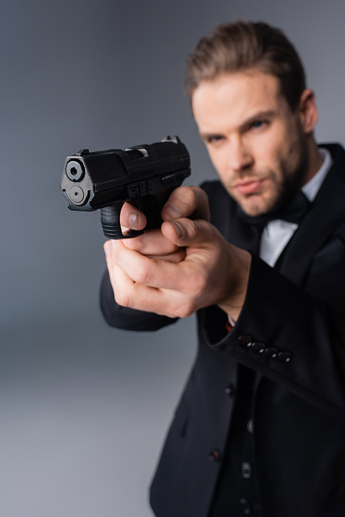 businessman in black suit aiming with gun on grey, blurred background