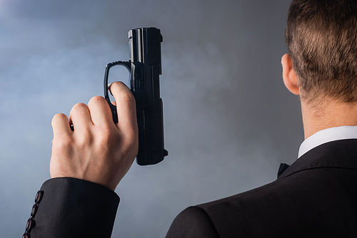 back view of businessman holding gun on grey background with smoke