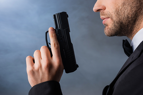 cropped view of young businessman with gun on grey background with smoke