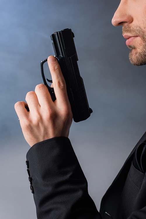 cropped view of businessman holding gun on grey background with smoke