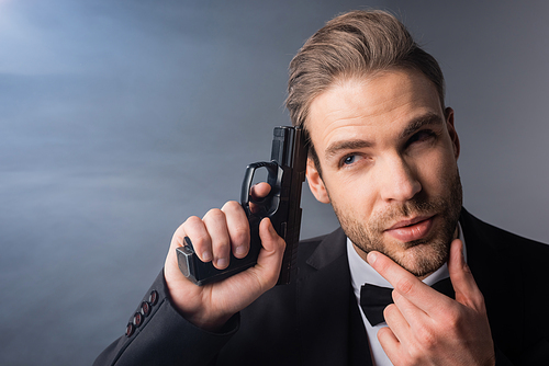 thoughtful businessman touching face while holding gun near head on grey background with smoke