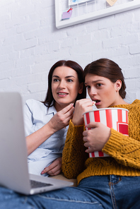 shocked teenage girl and mother watching movie on laptop in bedroom