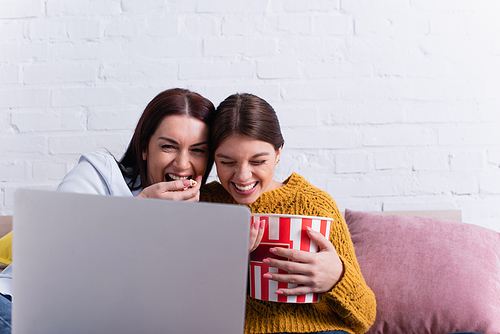 happy teenage girl and mother watching comedy movie on laptop and laughing in bedroom