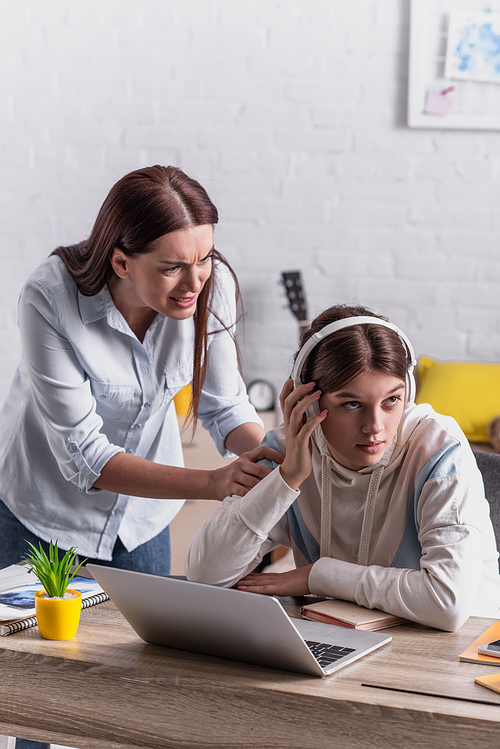 teenage girl in wireless headphones looking away near displeased mother