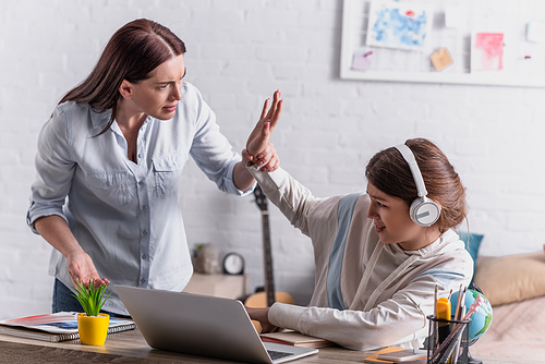 teenage girl in wireless headphones gesturing while quarrelling with mother