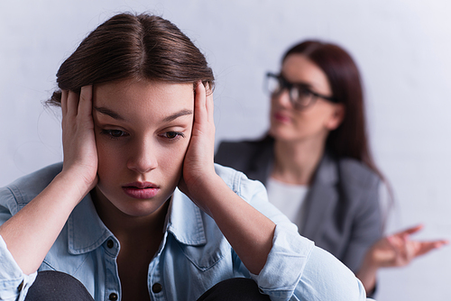 depressed teenage girl covering ears near psychologist on blurred background