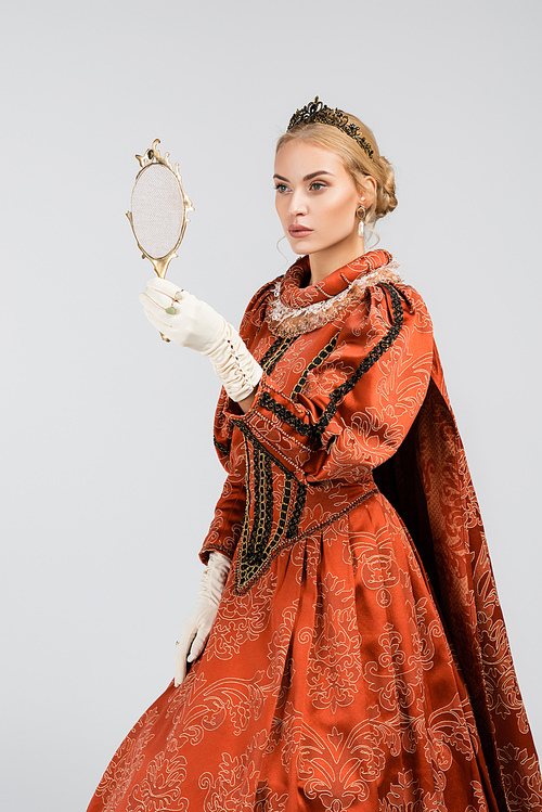 blonde queen in dress and crown and dress looking at mirror isolated on white