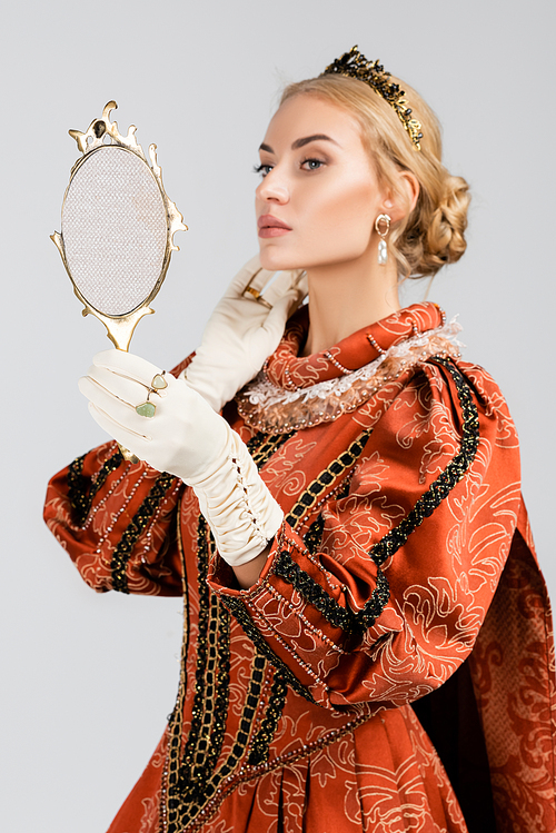 blonde queen in dress and crown looking at mirror isolated on white