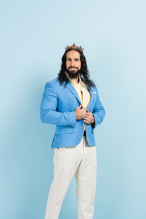 bearded hispanic man in crown and jacket posing on blue