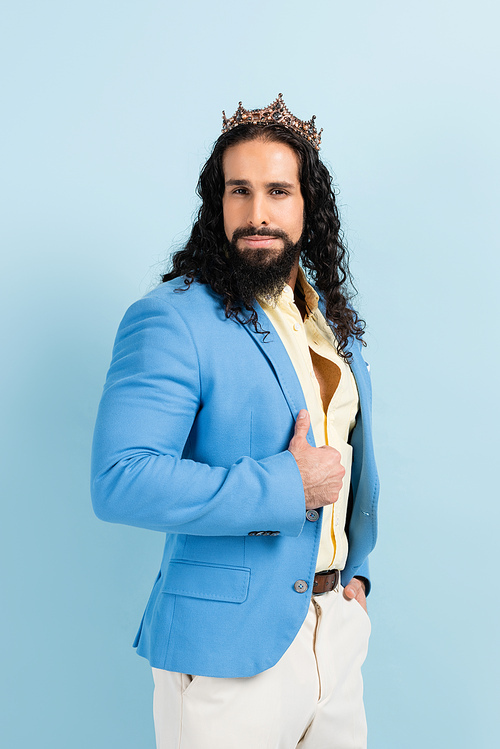 bearded hispanic man in crown and jacket posing isolated on blue