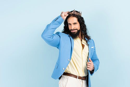 bearded and curly hispanic man in jacket adjusting crown isolated on blue