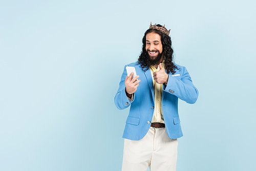 bearded hispanic man in jacket and crown showing thumb up during video call isolated on blue