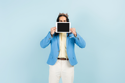 hispanic man in jacket and crown holding digital tablet with blank screen isolated on blue