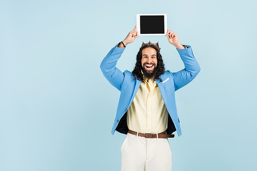 happy hispanic man in jacket and crown holding digital tablet with blank screen above head isolated on blue