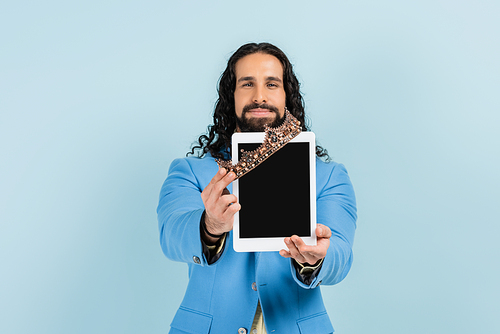 smiling  hispanic man in jacket holding digital tablet with blank screen and crown isolated on blue