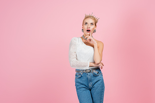 surprised blonde woman in luxury crown standing isolated on pink